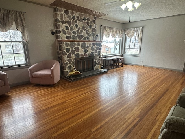 living room featuring a stone fireplace, ceiling fan, wood-type flooring, and a textured ceiling