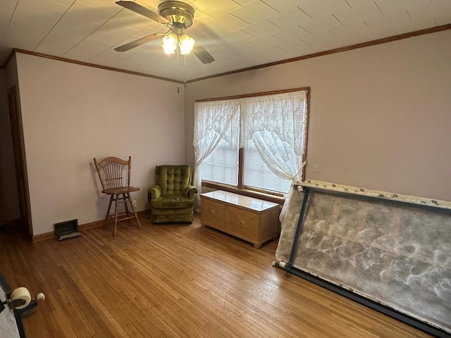 living area with ceiling fan, wood-type flooring, and crown molding