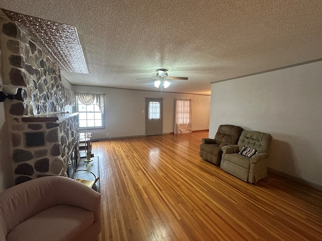 living room featuring hardwood / wood-style floors, ceiling fan, a stone fireplace, and a textured ceiling