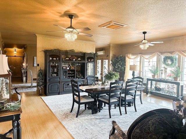 dining space featuring ceiling fan, wood finished floors, a textured ceiling, crown molding, and a wall unit AC