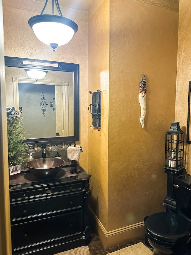 bathroom featuring toilet, a textured wall, baseboards, and vanity