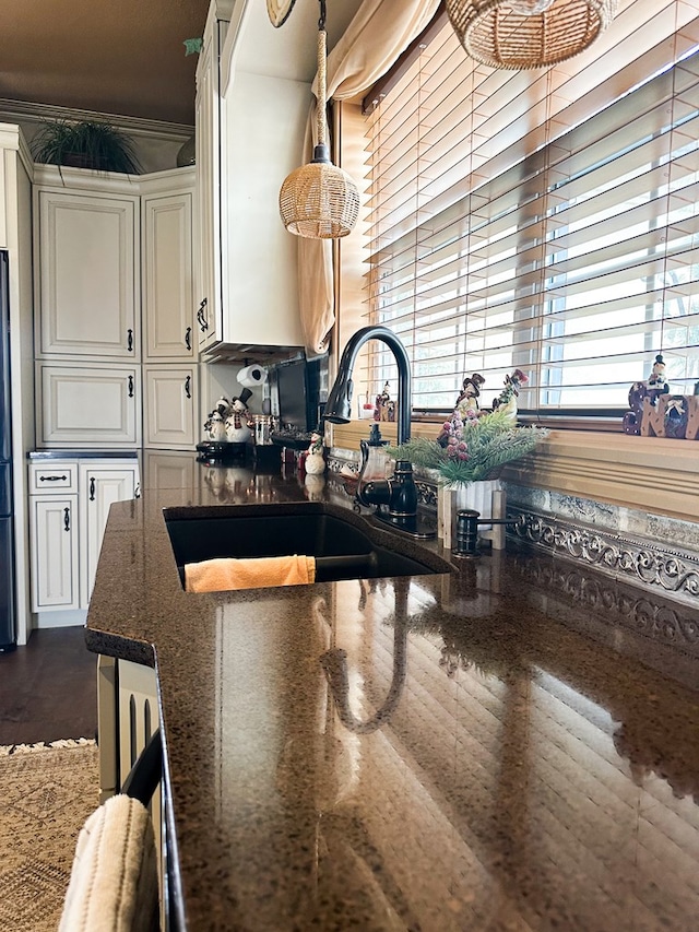 kitchen featuring a sink, white cabinets, freestanding refrigerator, dark stone countertops, and decorative light fixtures