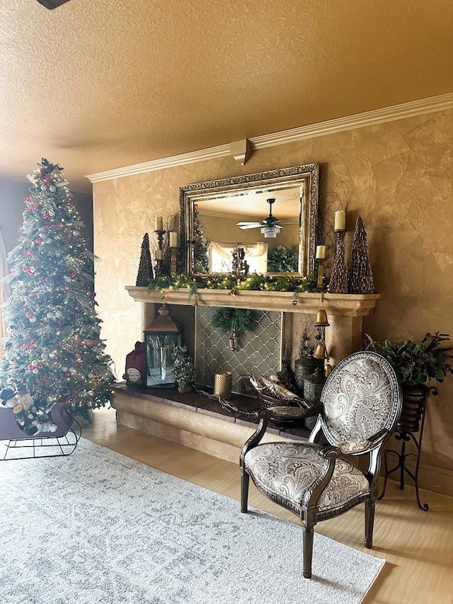 living area featuring ornamental molding, a textured ceiling, a ceiling fan, wood finished floors, and a glass covered fireplace