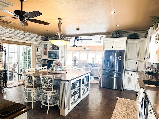 kitchen with stainless steel appliances, dark countertops, white cabinetry, a kitchen island, and brick wall