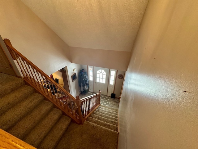 staircase with carpet, vaulted ceiling, and a textured ceiling