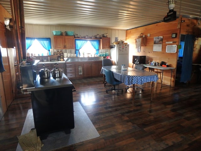 kitchen with wood walls, white fridge, dark wood-type flooring, and a kitchen island