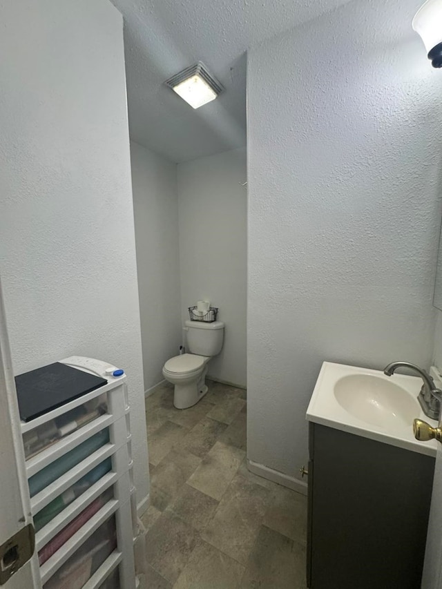 half bathroom with a textured wall, vanity, baseboards, and toilet