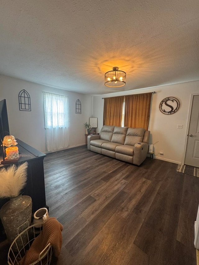 living room with dark wood-type flooring, a textured ceiling, a notable chandelier, and baseboards