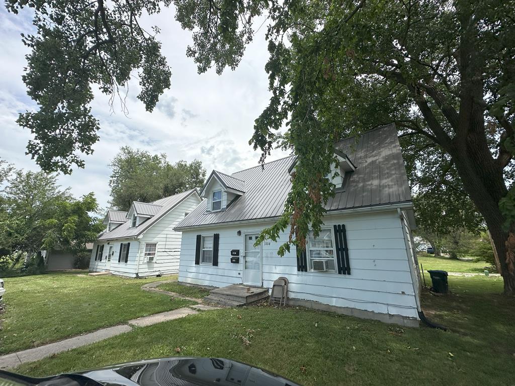 view of front facade with cooling unit, a front lawn, and metal roof