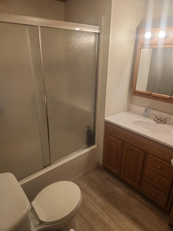 full bathroom featuring toilet, vanity, wood-type flooring, and combined bath / shower with glass door