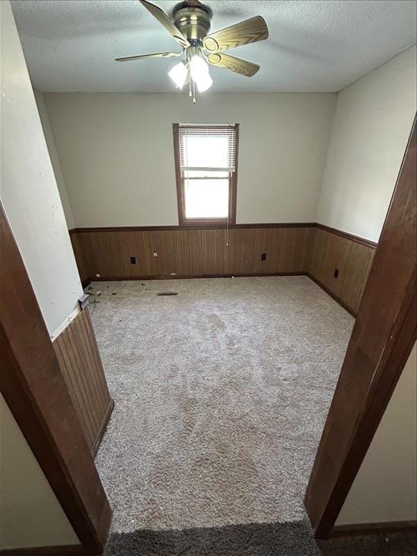 803 Coates St, Macon, MO 63552 - carpeted empty room with a wainscoted wall, wooden walls, ceiling fan, and a textured ceiling