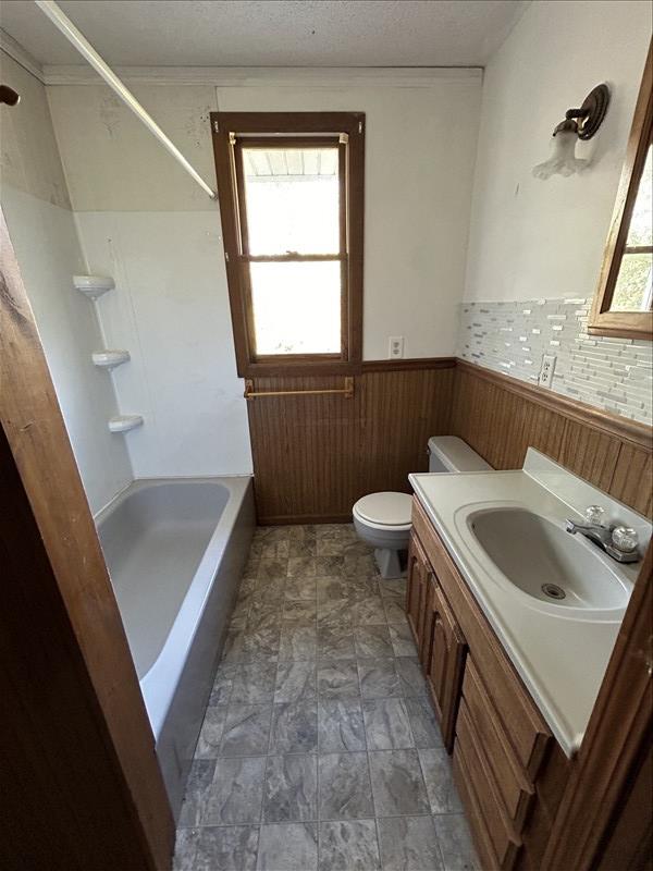 803 Coates St, Macon, MO 63552 - bathroom with a wainscoted wall, toilet, vanity, wooden walls, and a textured ceiling