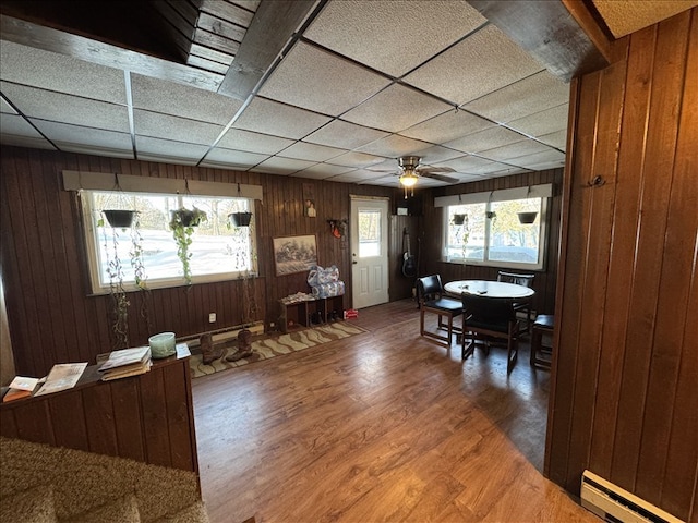 dining area featuring ceiling fan, a drop ceiling, a baseboard radiator, and hardwood / wood-style flooring