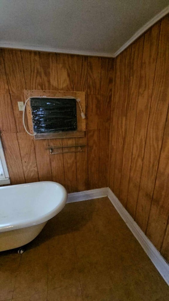 bathroom featuring wood walls, baseboards, and a soaking tub