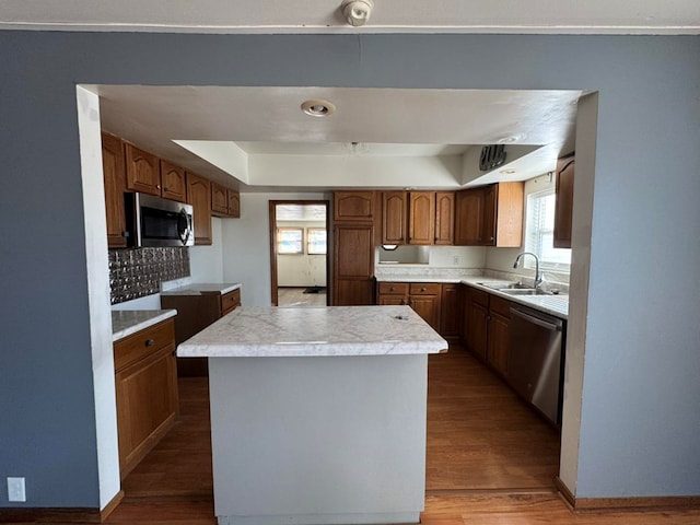 kitchen featuring wood finished floors, a sink, appliances with stainless steel finishes, a center island, and a raised ceiling