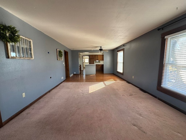 unfurnished living room featuring baseboards, a ceiling fan, and light colored carpet