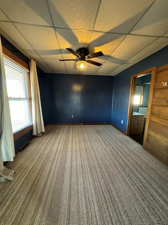 carpeted empty room with baseboards, ceiling fan, visible vents, and a drop ceiling