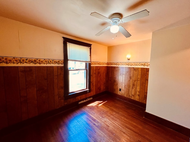 unfurnished room with ceiling fan, wood walls, and dark wood-type flooring