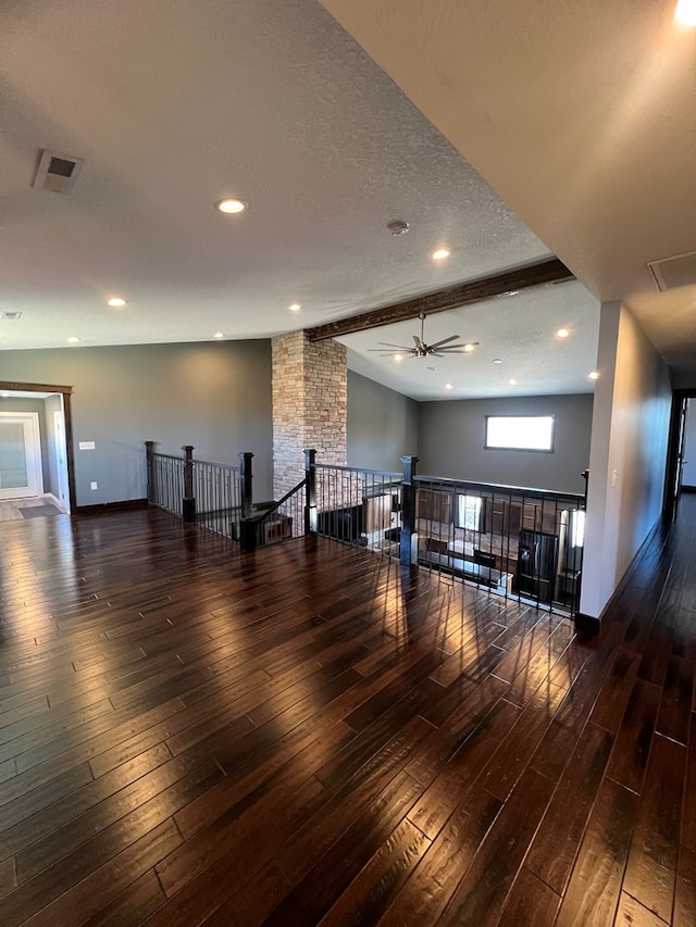 empty room with vaulted ceiling with beams, a textured ceiling, dark wood finished floors, and a ceiling fan