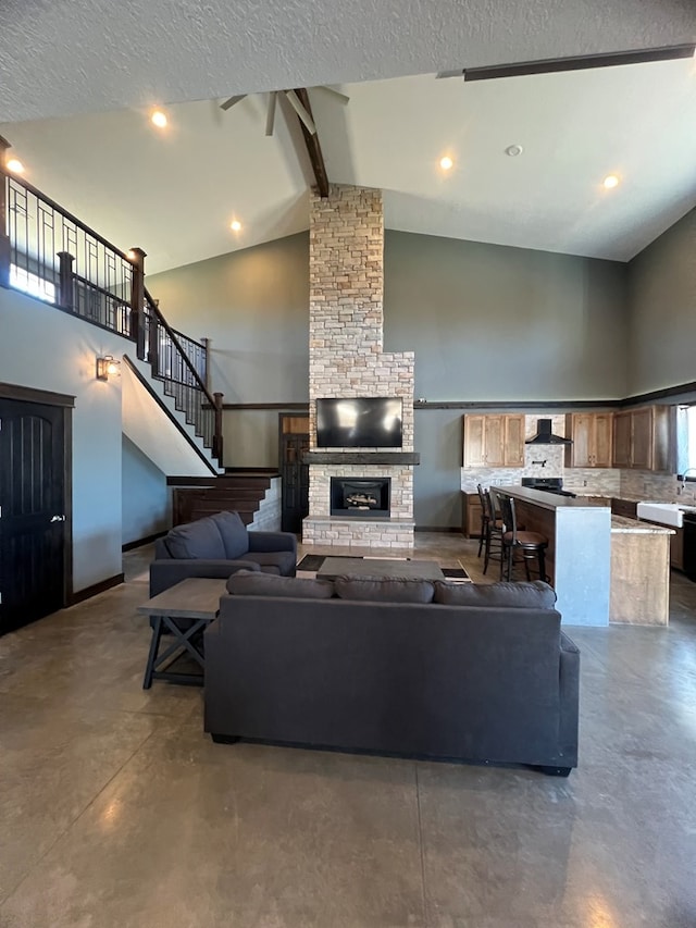 living area with finished concrete flooring, stairway, beamed ceiling, a fireplace, and high vaulted ceiling