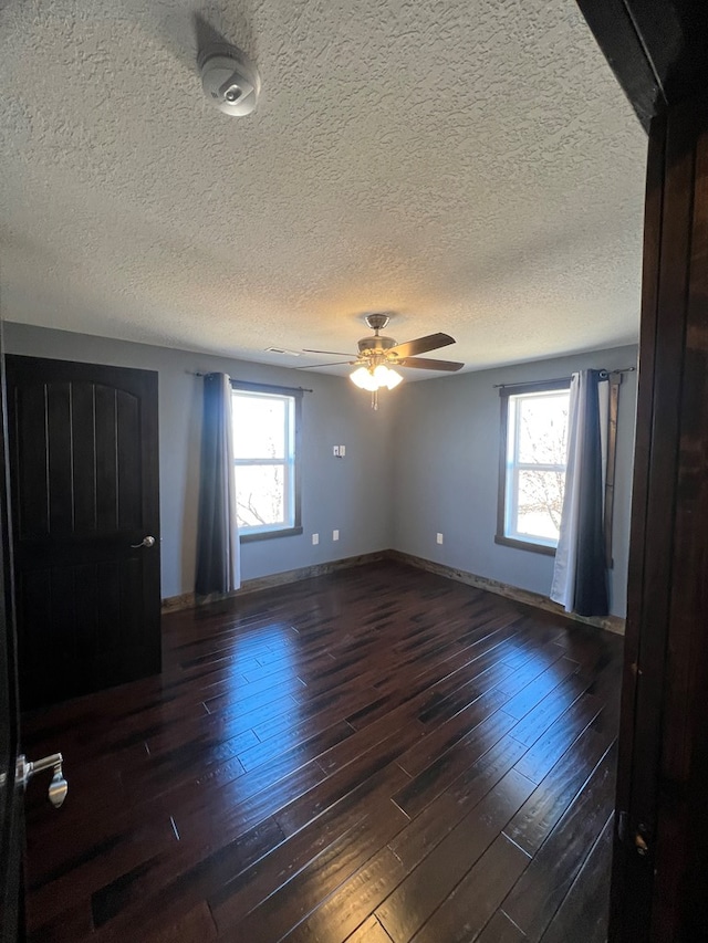 empty room with a wealth of natural light, ceiling fan, baseboards, and dark wood-type flooring