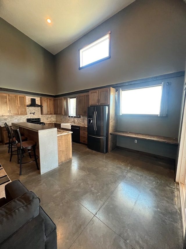 kitchen with wall chimney exhaust hood, decorative backsplash, a high ceiling, black appliances, and a kitchen breakfast bar