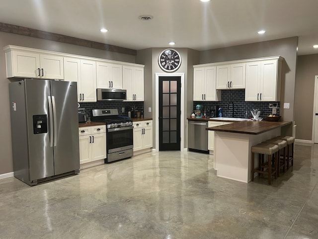 kitchen with decorative backsplash, a breakfast bar, stainless steel appliances, sink, and white cabinetry