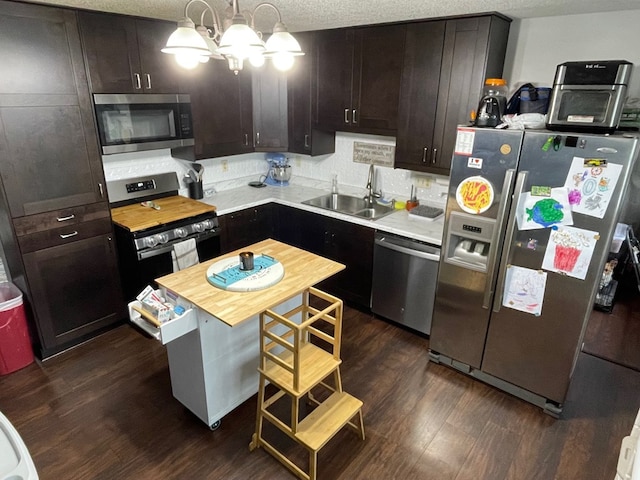 kitchen with a sink, a textured ceiling, appliances with stainless steel finishes, an inviting chandelier, and dark wood-style flooring