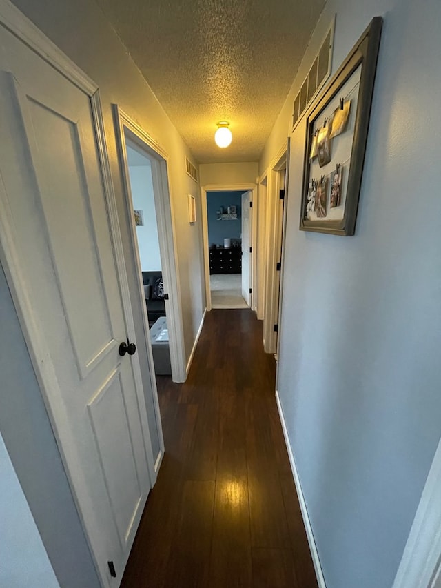 corridor featuring dark wood-style floors, visible vents, a textured ceiling, and baseboards