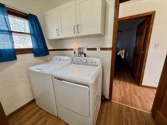 clothes washing area with cabinet space, tile walls, washing machine and clothes dryer, and wood finished floors