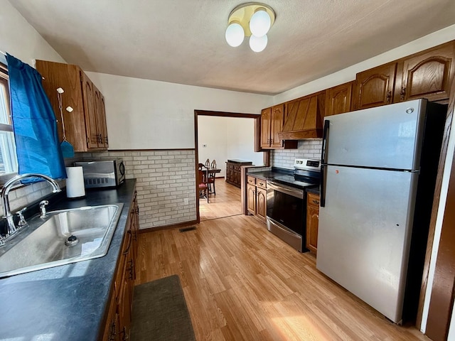 kitchen with dark countertops, light wood-style flooring, appliances with stainless steel finishes, premium range hood, and a sink