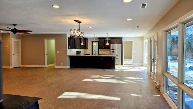 kitchen featuring pendant lighting, ceiling fan with notable chandelier, sink, stainless steel fridge, and dark brown cabinetry