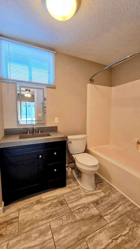 full bathroom featuring vanity, bathtub / shower combination, a textured ceiling, and toilet