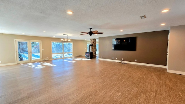 unfurnished living room with ceiling fan, a wood stove, a textured ceiling, and french doors