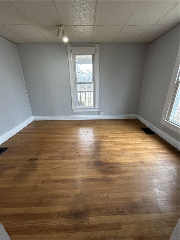 unfurnished room with wood-type flooring, a healthy amount of sunlight, and a drop ceiling