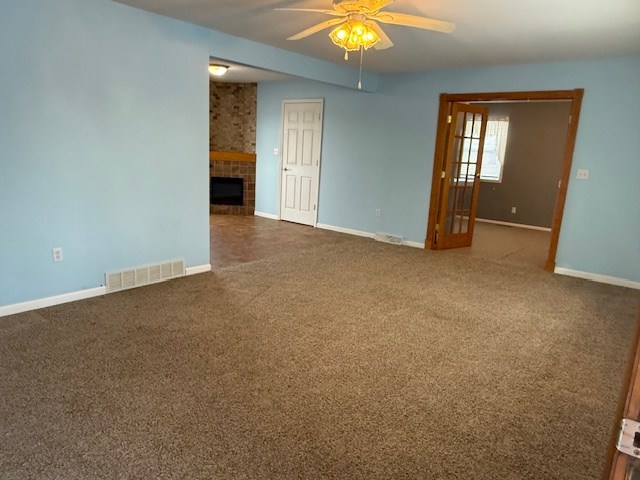 empty room with dark carpet, a fireplace, and ceiling fan