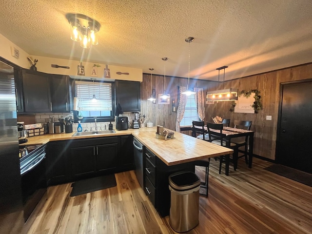 kitchen featuring wood counters, appliances with stainless steel finishes, kitchen peninsula, sink, and hanging light fixtures