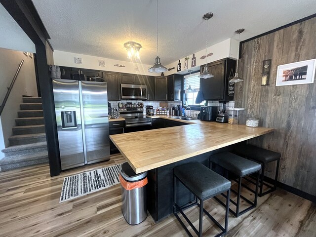 639 Missouri Ave, Chillicothe, MO 64601 - kitchen with appliances with stainless steel finishes, light wood-style flooring, a peninsula, a breakfast bar, and wood walls