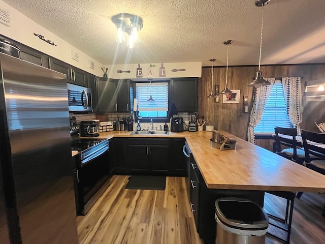 kitchen featuring wooden counters, sink, a textured ceiling, appliances with stainless steel finishes, and decorative light fixtures