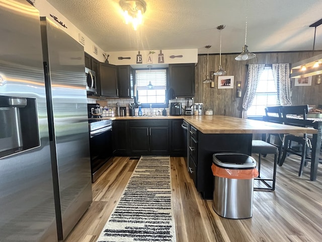 639 Missouri Ave, Chillicothe, MO 64601 - kitchen with appliances with stainless steel finishes, plenty of natural light, a breakfast bar area, light wood-type flooring, and wooden walls