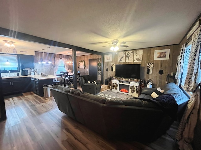 living room featuring ceiling fan, wood-type flooring, a textured ceiling, and wooden walls