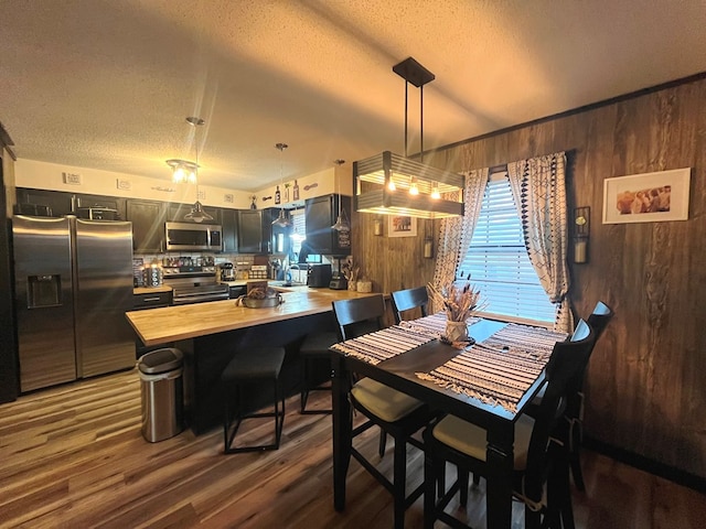 dining room with a textured ceiling, dark hardwood / wood-style flooring, sink, and wooden walls