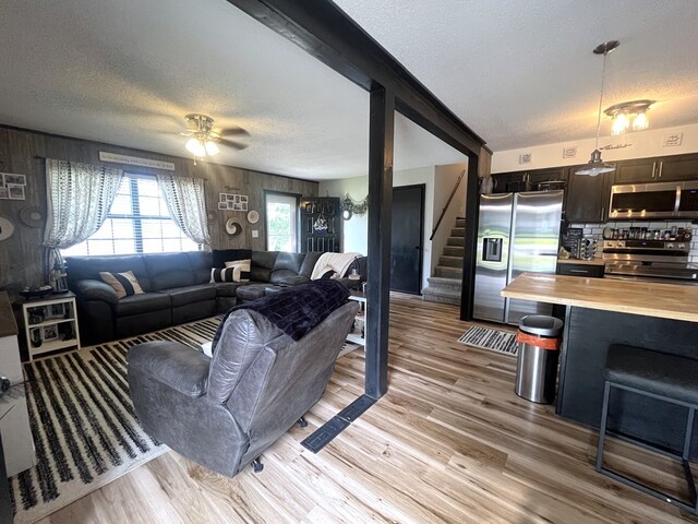 639 Missouri Ave, Chillicothe, MO 64601 - living room featuring a textured ceiling, stairs, light wood-style floors, ceiling fan, and wood walls
