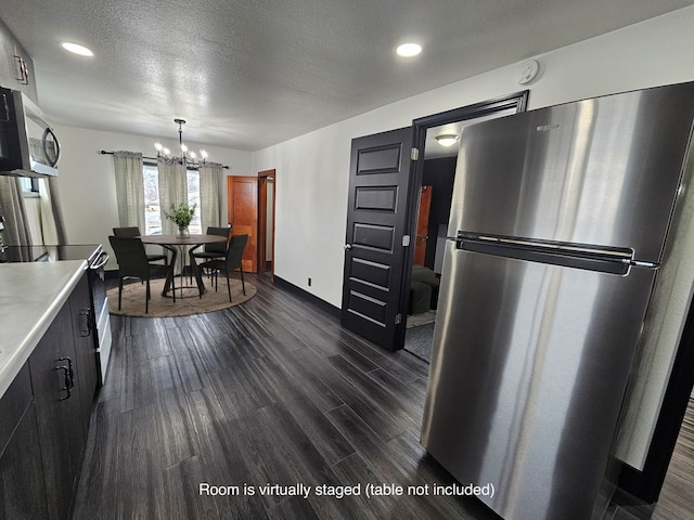 kitchen featuring a textured ceiling, light countertops, a chandelier, appliances with stainless steel finishes, and dark wood-style floors