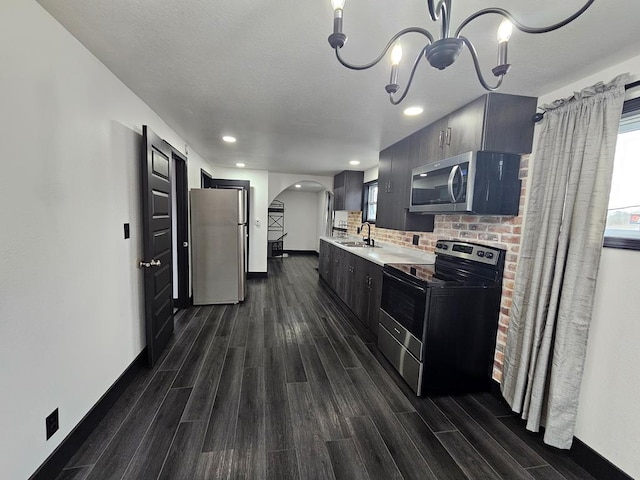 kitchen with light countertops, dark wood-style flooring, a sink, arched walkways, and appliances with stainless steel finishes