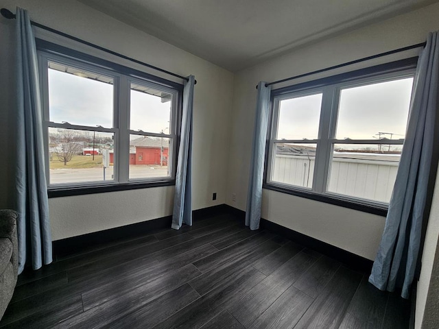 empty room featuring dark wood finished floors, a wealth of natural light, and baseboards
