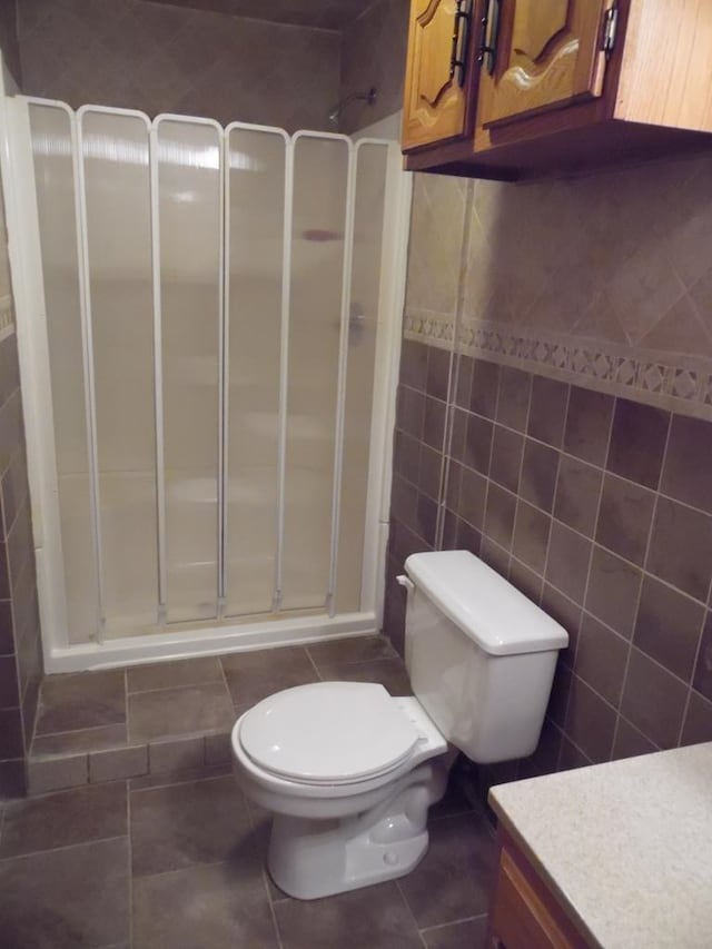 bathroom featuring vanity, toilet, tile walls, and a shower with shower door