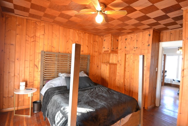 bedroom featuring ceiling fan, dark hardwood / wood-style flooring, wood ceiling, and wooden walls