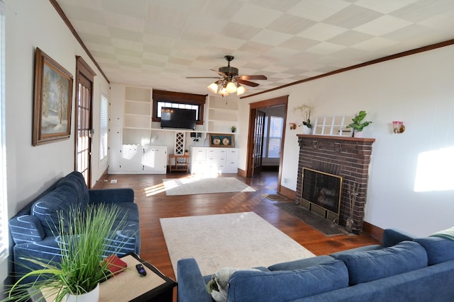 living room with built in shelves, ceiling fan, dark wood-type flooring, and a brick fireplace