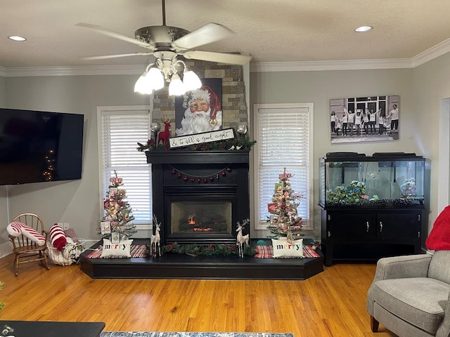 living room featuring hardwood / wood-style floors, a large fireplace, ceiling fan, and crown molding